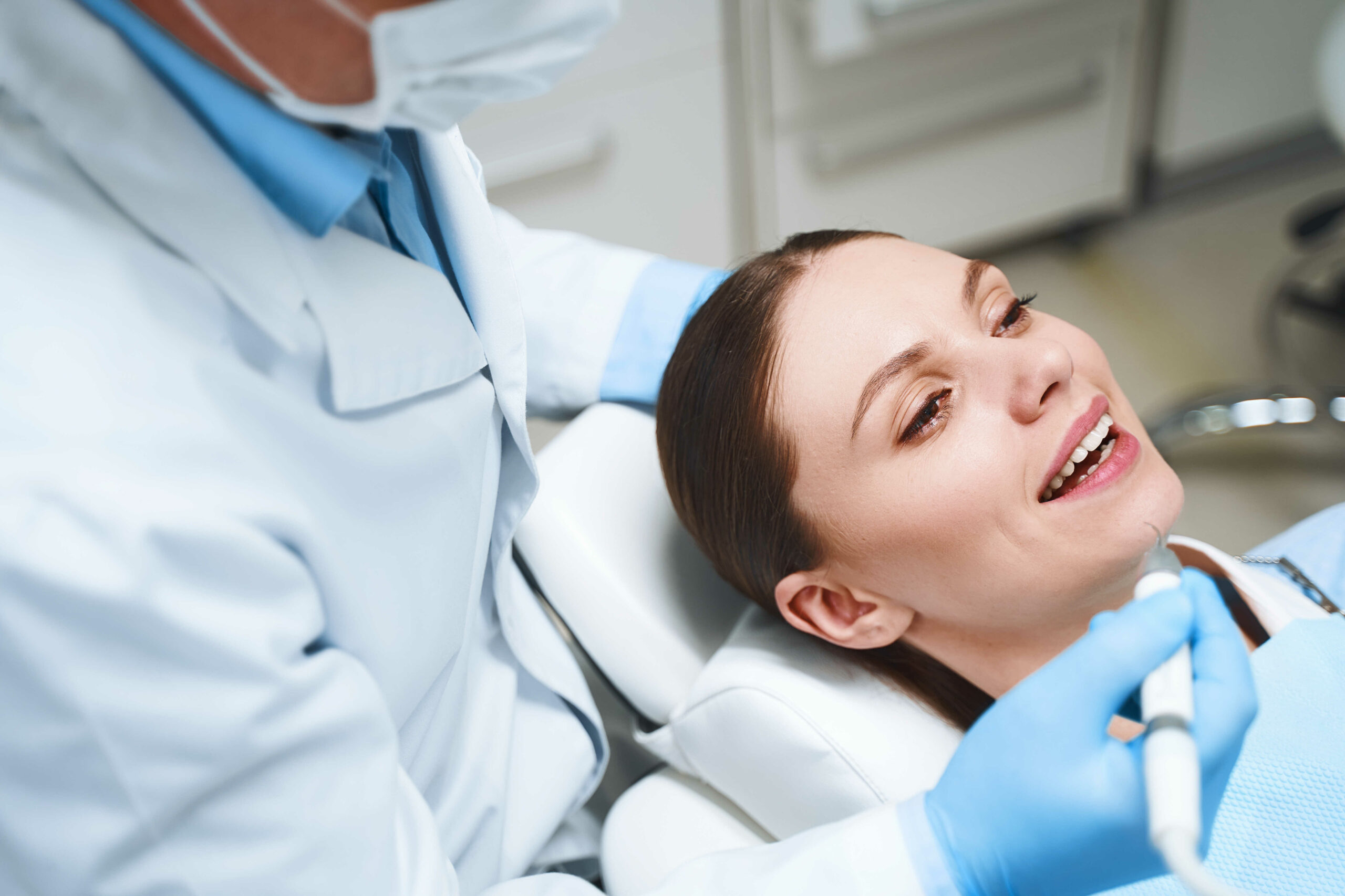 Cheerful woman is lying in chair while being treated by dentist with instrument in Warren, MI